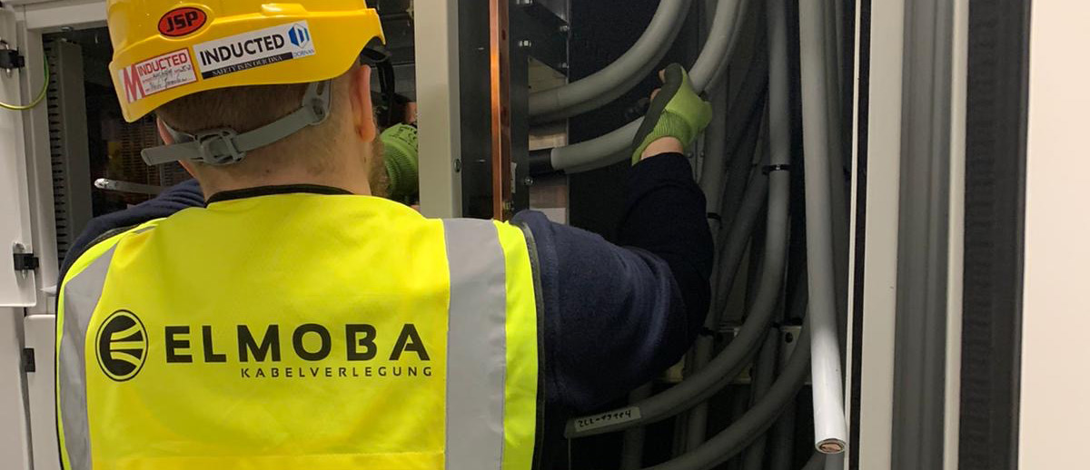Mitarbeiter in Schutzausrüstung schließt Kabel an - Elmoba Kabelverlegung GmbH in Marl und Chur